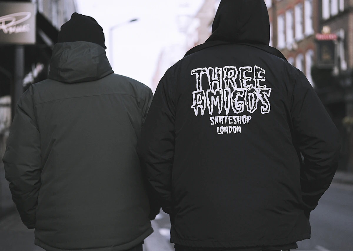 Two people wearing dark outer layers on a city street, one with lettering on the back