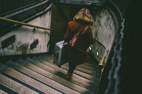woman walking on stairway while holding luggage