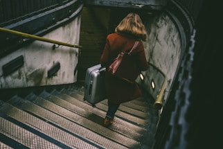 woman walking on stairway while holding luggage