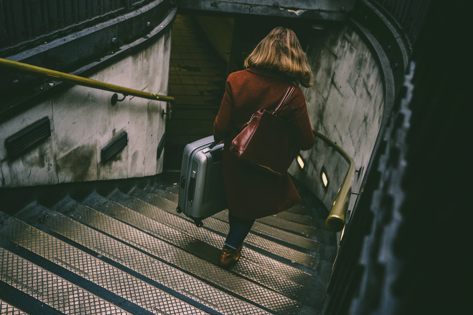 A traveller carries a suitcase down a long flight of station stairs.