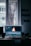 A computer monitor displaying video editing software with a burning flame on the screen. The setup is in a dimly lit room with a wooden desk, keyboard, and window in the background. There are photographs hanging on the wall.
