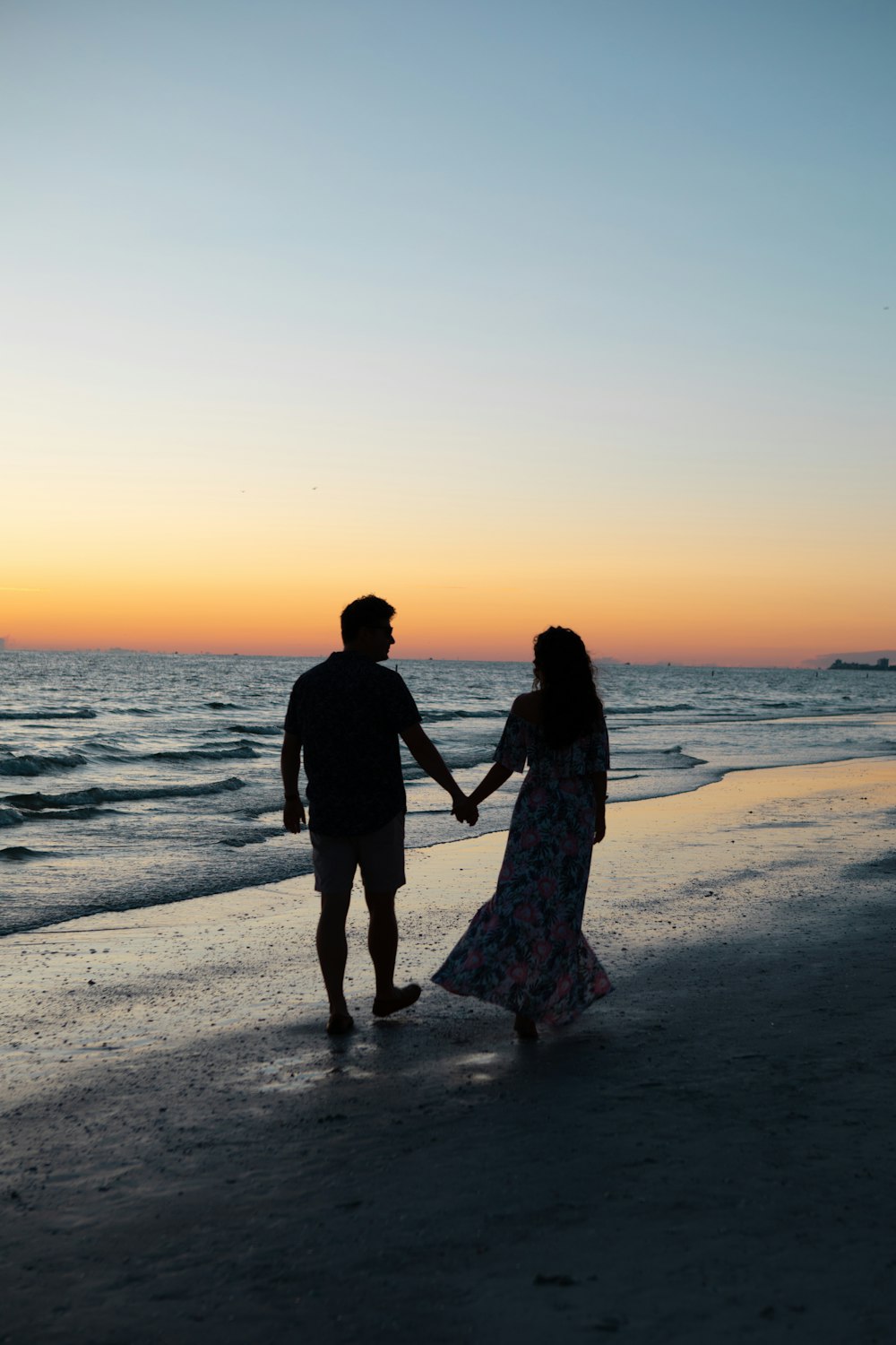 photography of man and woman holding hands each other while walking beside seashore