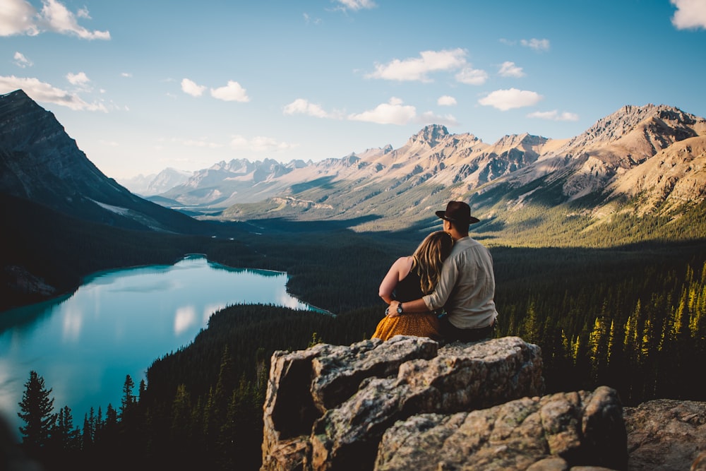 woman and man sitting on the cliff facing the river