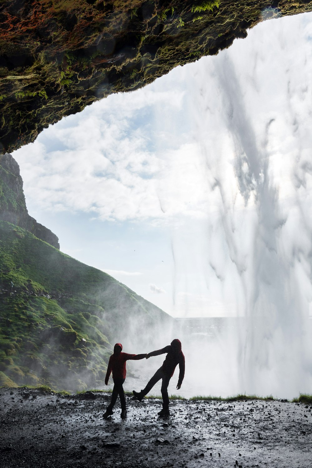 silhouette of man and woman holding each other hands under the cave with waterfalls