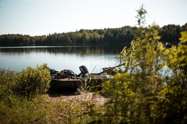 A boat equipped with Arcooli fishing gear floating on a serene lake surrounded by trees.