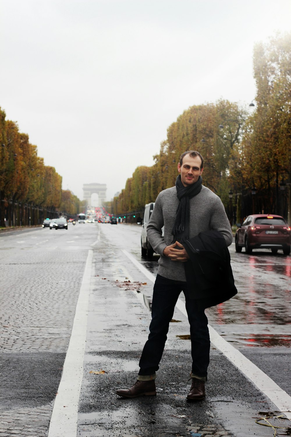 man wearing gray sweater with black scarf and black jeans standing on street