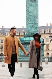 man wearing beige trench coat and black pants walking with woman holding hands wearing gray trench coat aND GRAY MINISKIRT