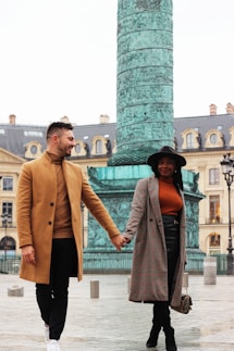 man wearing beige trench coat and black pants walking with woman holding hands wearing gray trench coat aND GRAY MINISKIRT