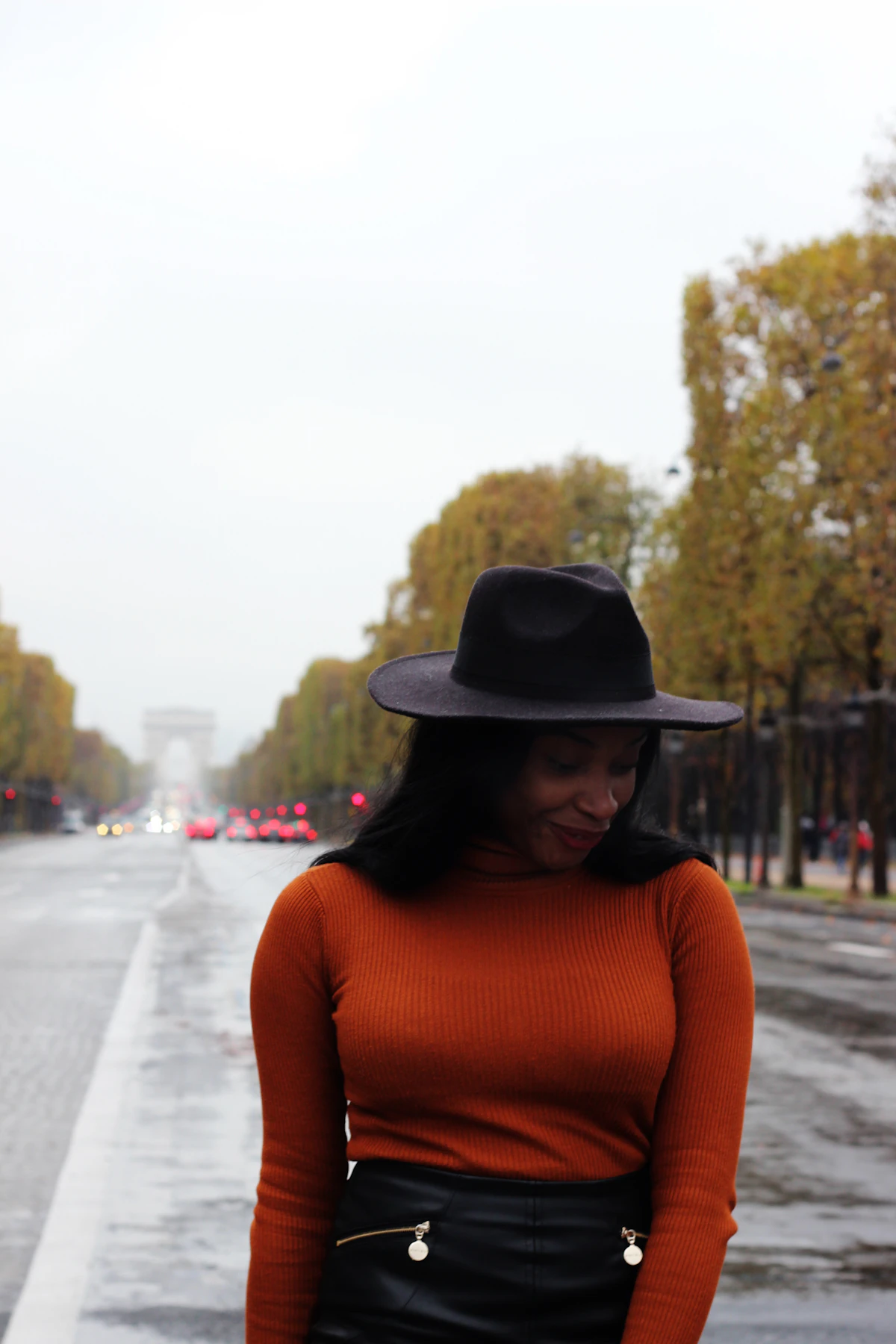 Woman in a rust knit sweater and wide hat walking down a street