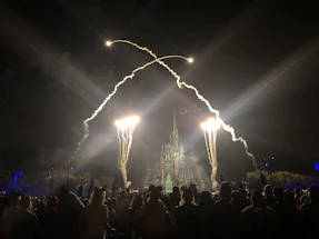Una familia feliz disfrutando de un parque temático de Disney con castillos y fuegos artificiales al atardecer.