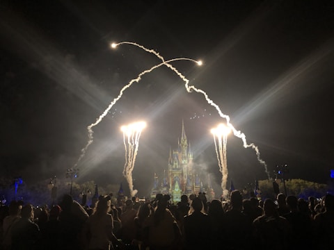 Children and adults smiling in front of Cinderella’s Castle at a Disney park, fireworks lighting the night sky.