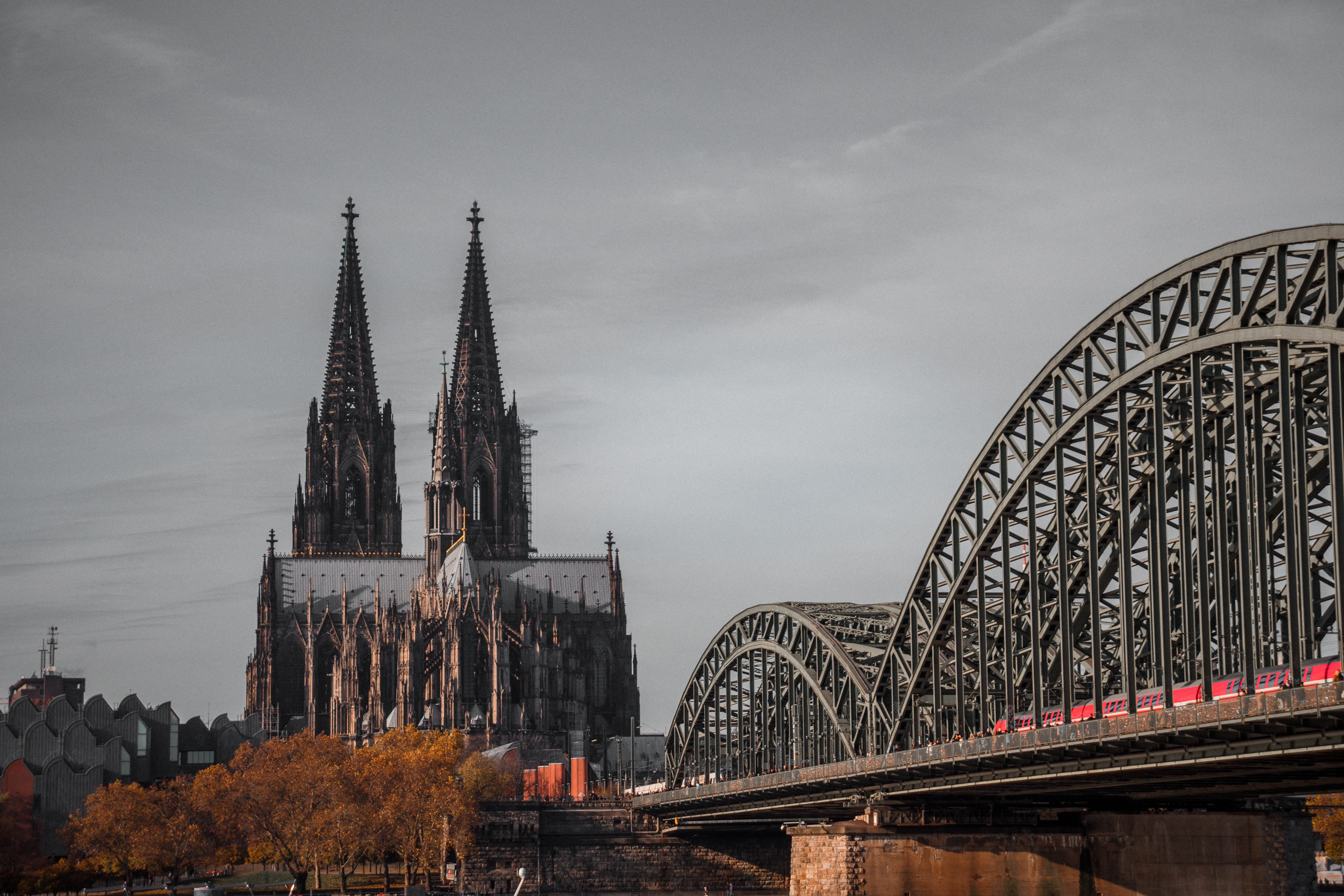 Cologne Cathedral's spires rise beside the Hohenzollern Bridge as a train crosses in warm dusk light.