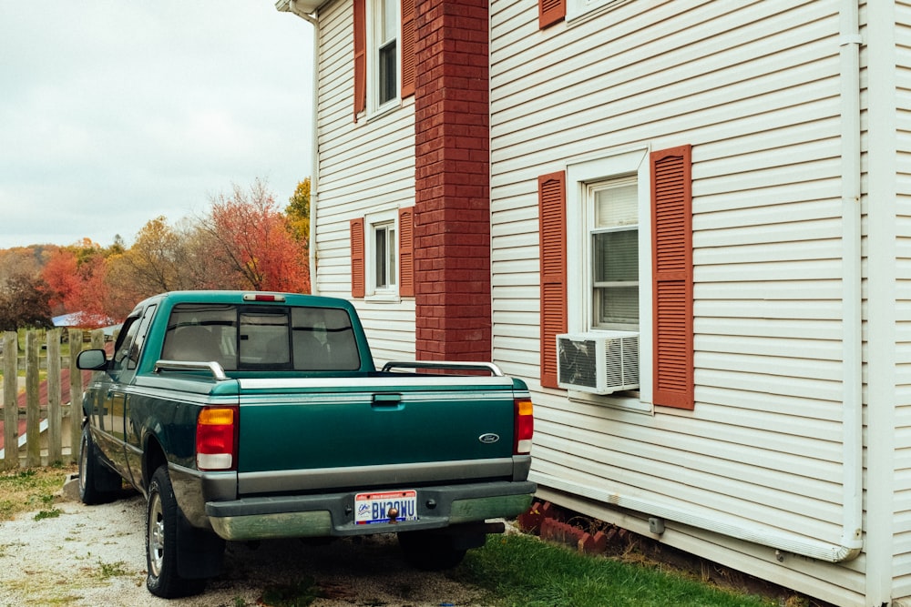 green crew cab pickup truck beside house