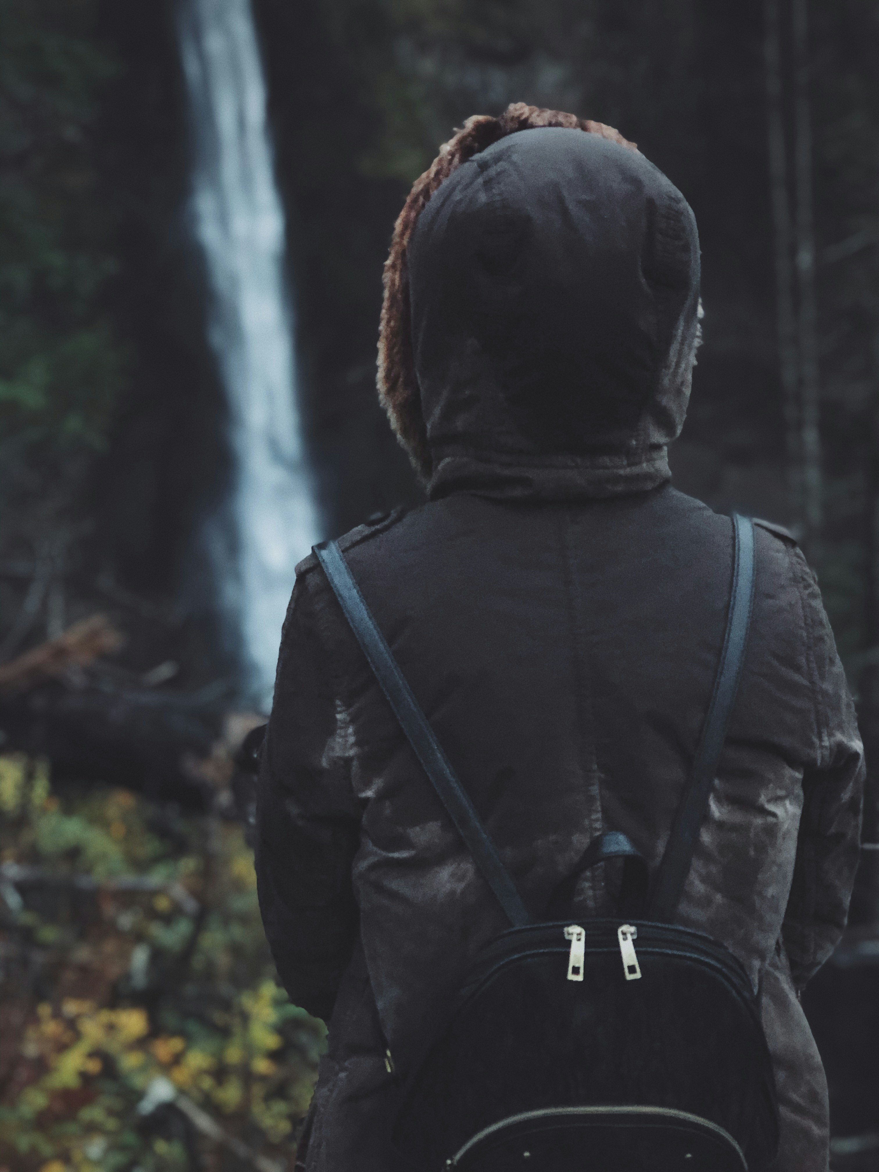 A moody shot of a woman admiring a misty waterfall with rain soaking her coat.