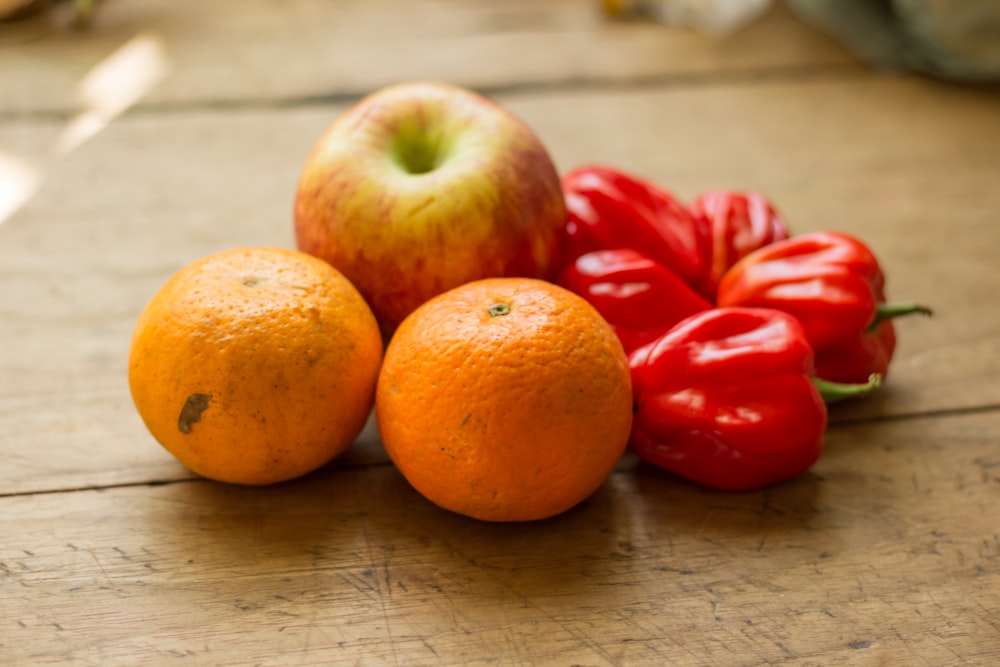 2 oranges, apple, and 5 peppers on wooden surface