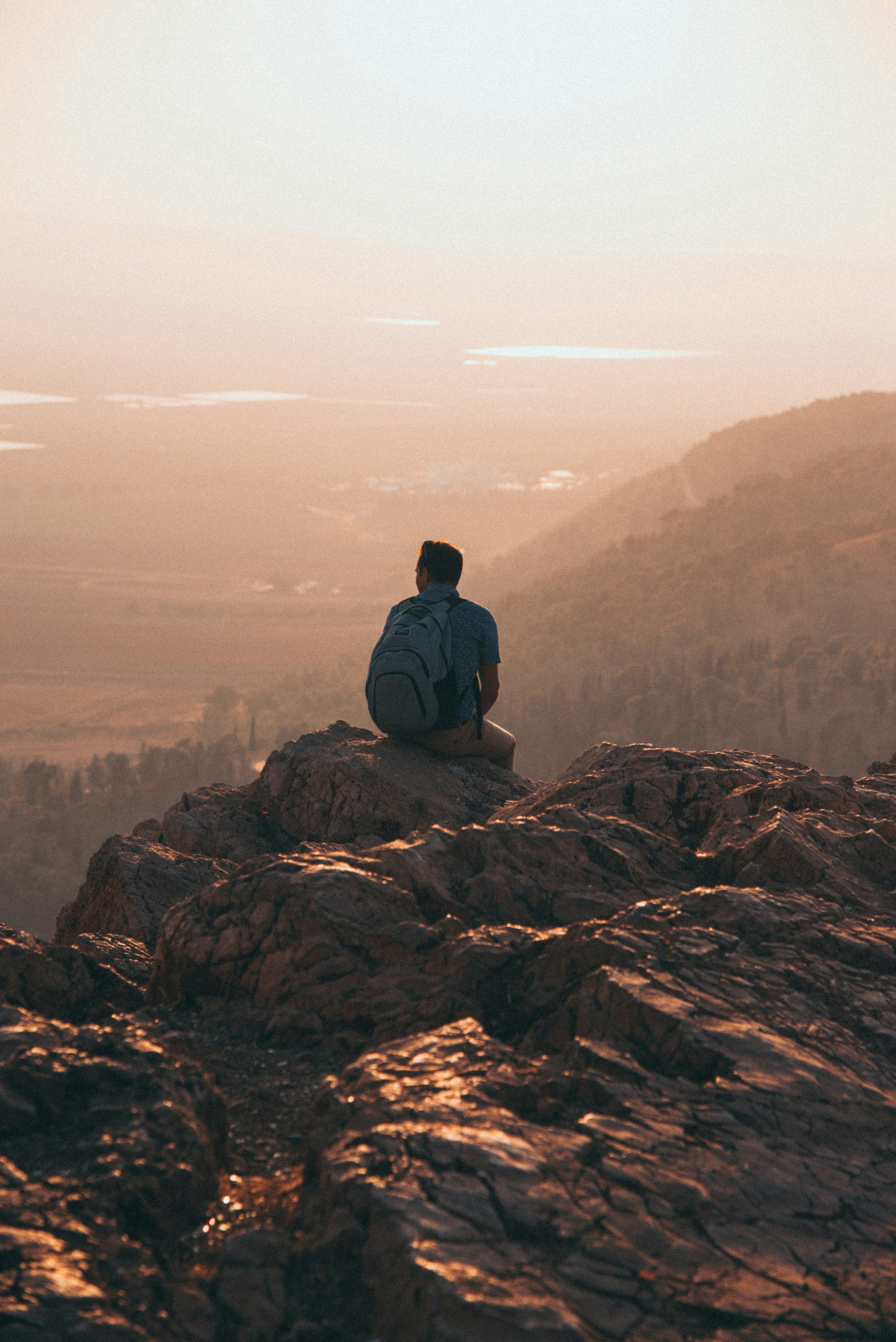 man wearing blue shirt and carrying backpack sitting on rock