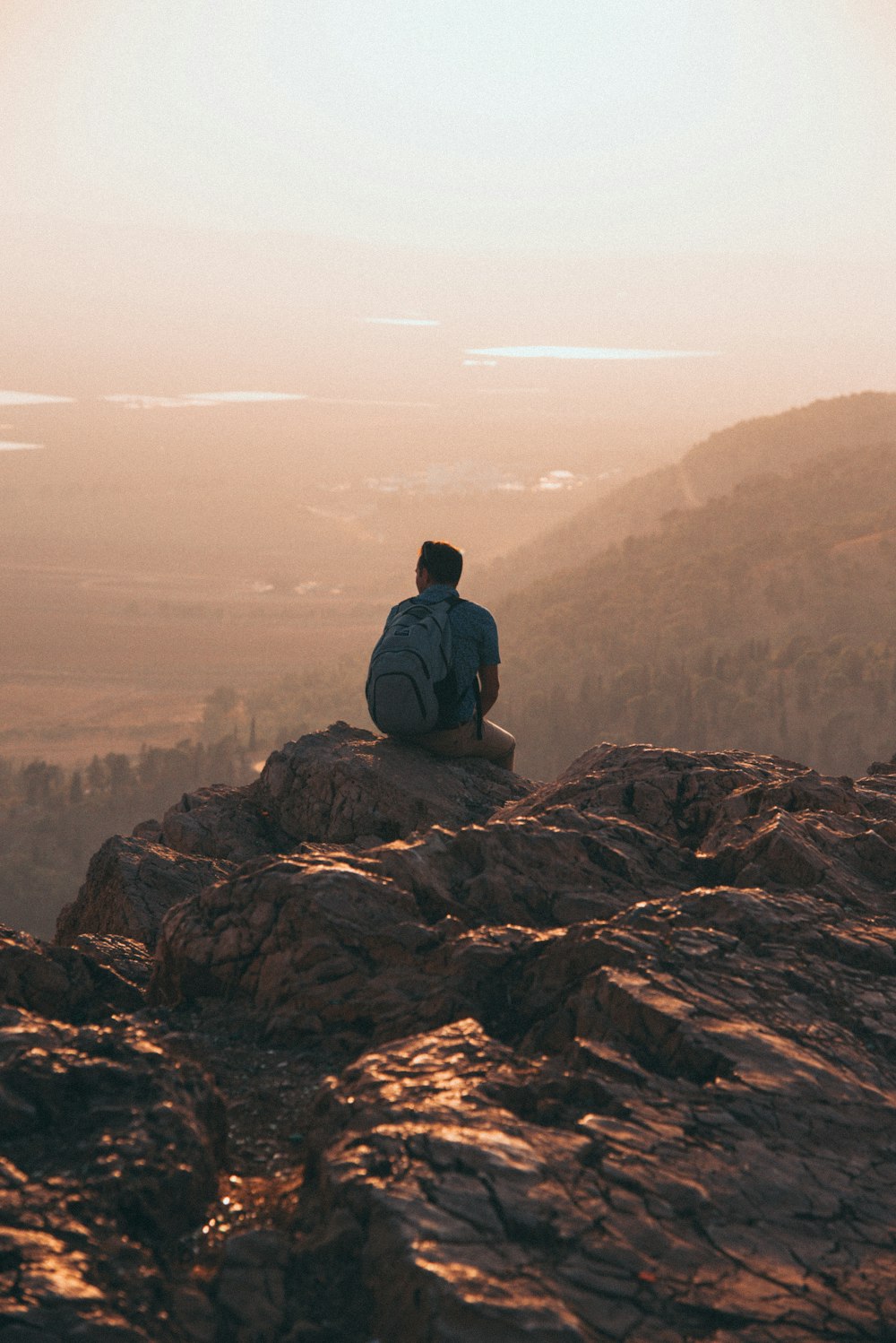 man wearing blue shirt and carrying backpack sitting on rock