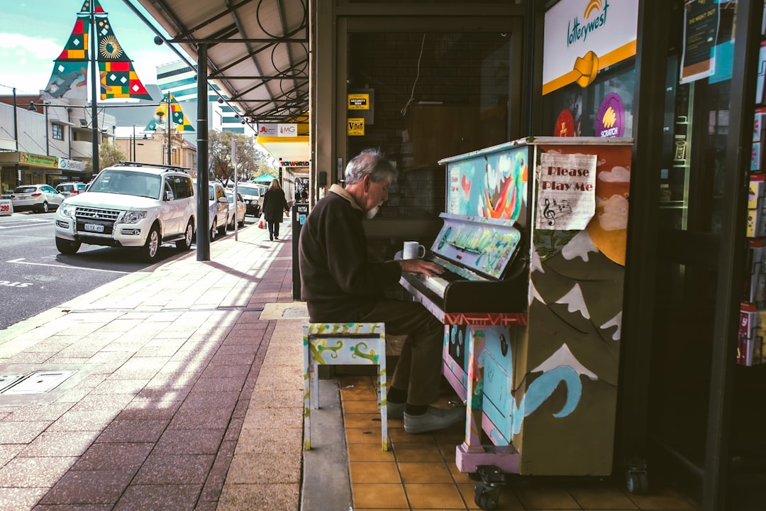 man playing piano beside building and sidewalk during day