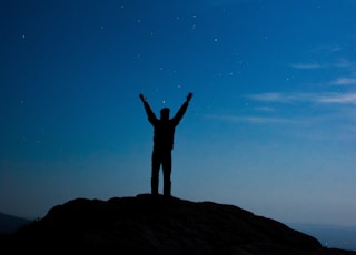 silhouette of man standing on hill with arms wide open