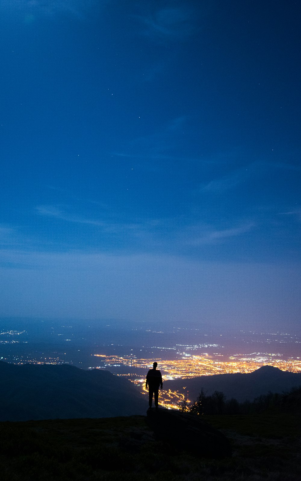 Mann steht auf dem Gipfel eines Berges über den Lichtern in der Stadt