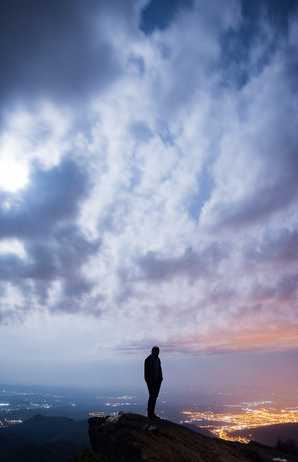 uomo in piedi sulla scogliera con vista del paesaggio urbano sotto cielo nuvoloso