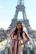 A happy family posing in front of the Eiffel Tower, smiling under a clear blue sky.