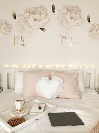 white heart cushion pillow near coffee in mug, white book, and cookies on tray on top of white bed