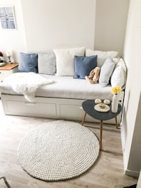 blue and white pillows on white couch and round white area mat on floor