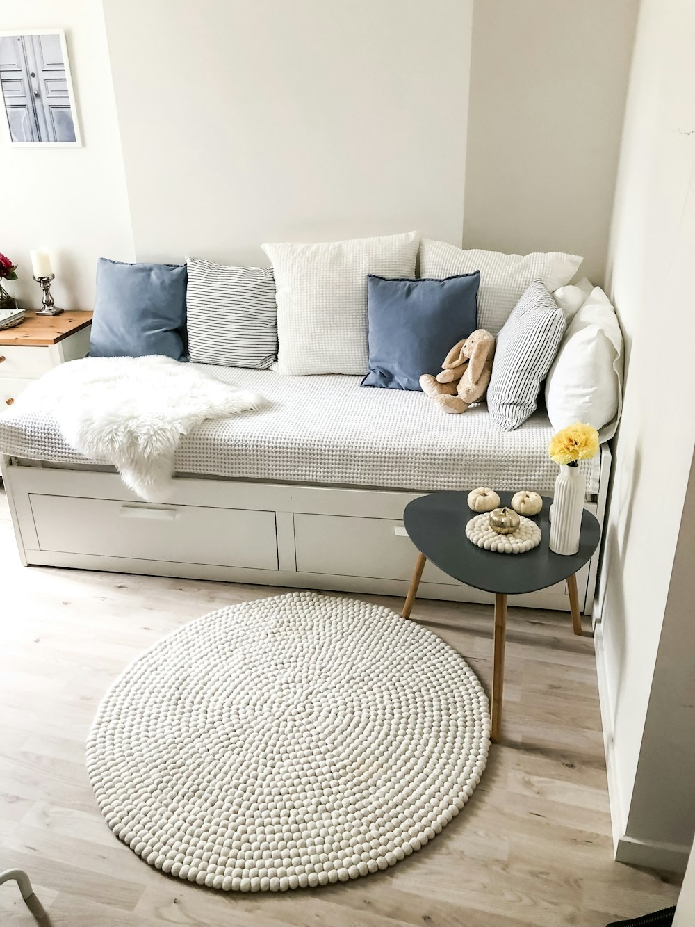 blue and white pillows on white couch and round white area mat on floor