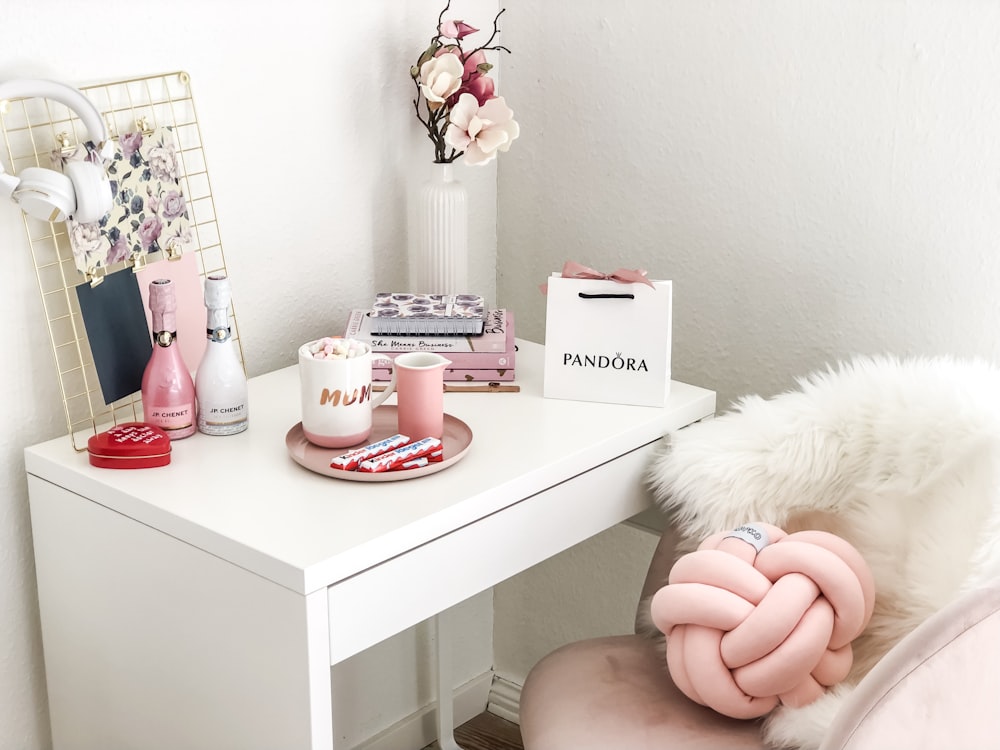 white and pink mug near chocolate packs, Pandora shopping bag, books, vases, and white and pink flowers in vase on white wooden table