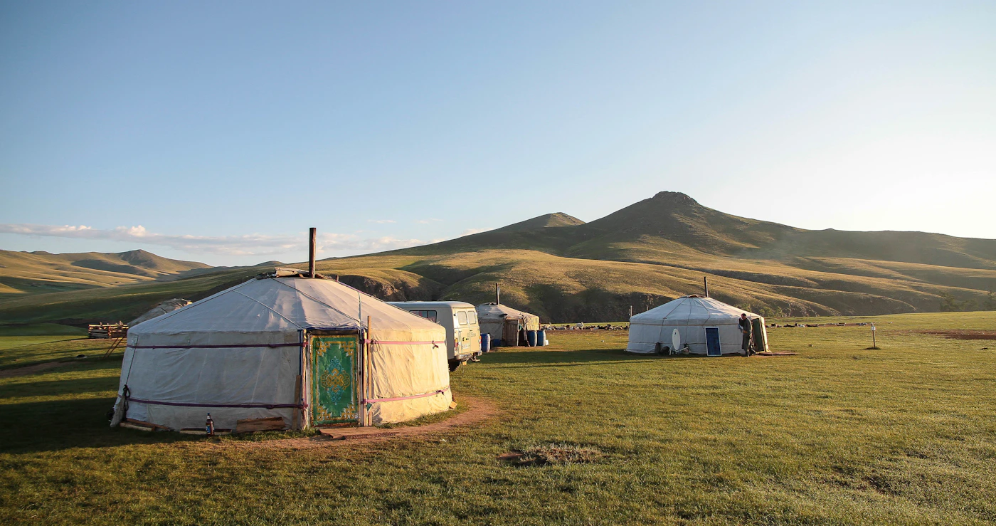 Traditional white Mongolian gers (yurts) scattered across the vast green steppe under a wide blue sky