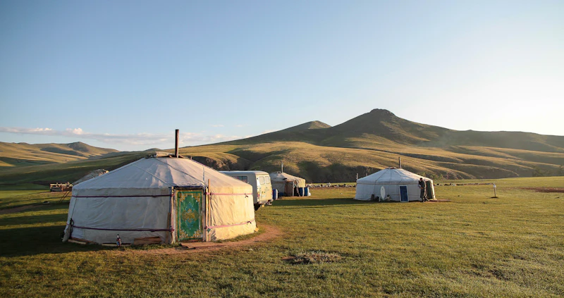 Traditional white Mongolian gers (yurts) scattered across the vast green steppe under a wide blue sky