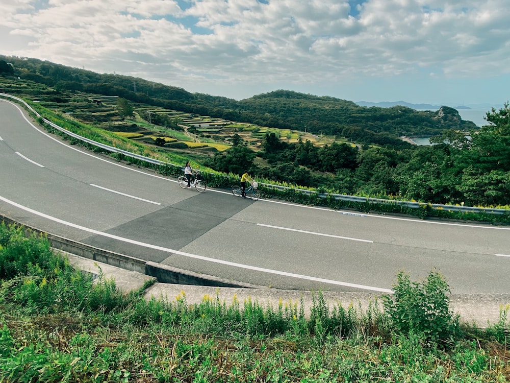 view photography of two persons riding bicycles on road during daytime