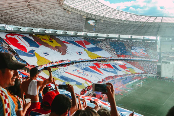 A vibrant photo of a lively football tournament crowd enjoying the event with banners and DJ booth in the background.