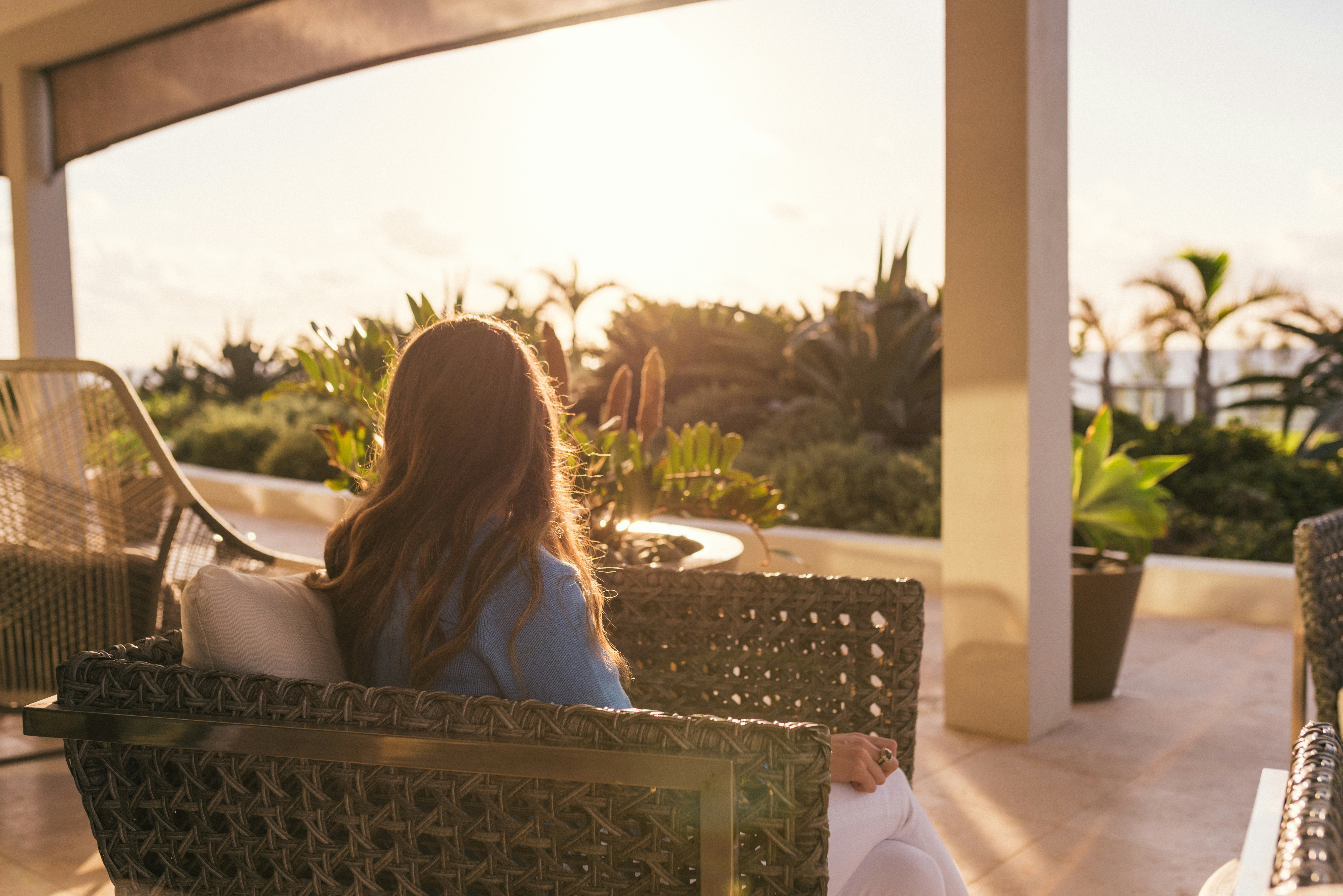 woman wearing blue shirt sitting on gray wicker chair bermuda zoom background
