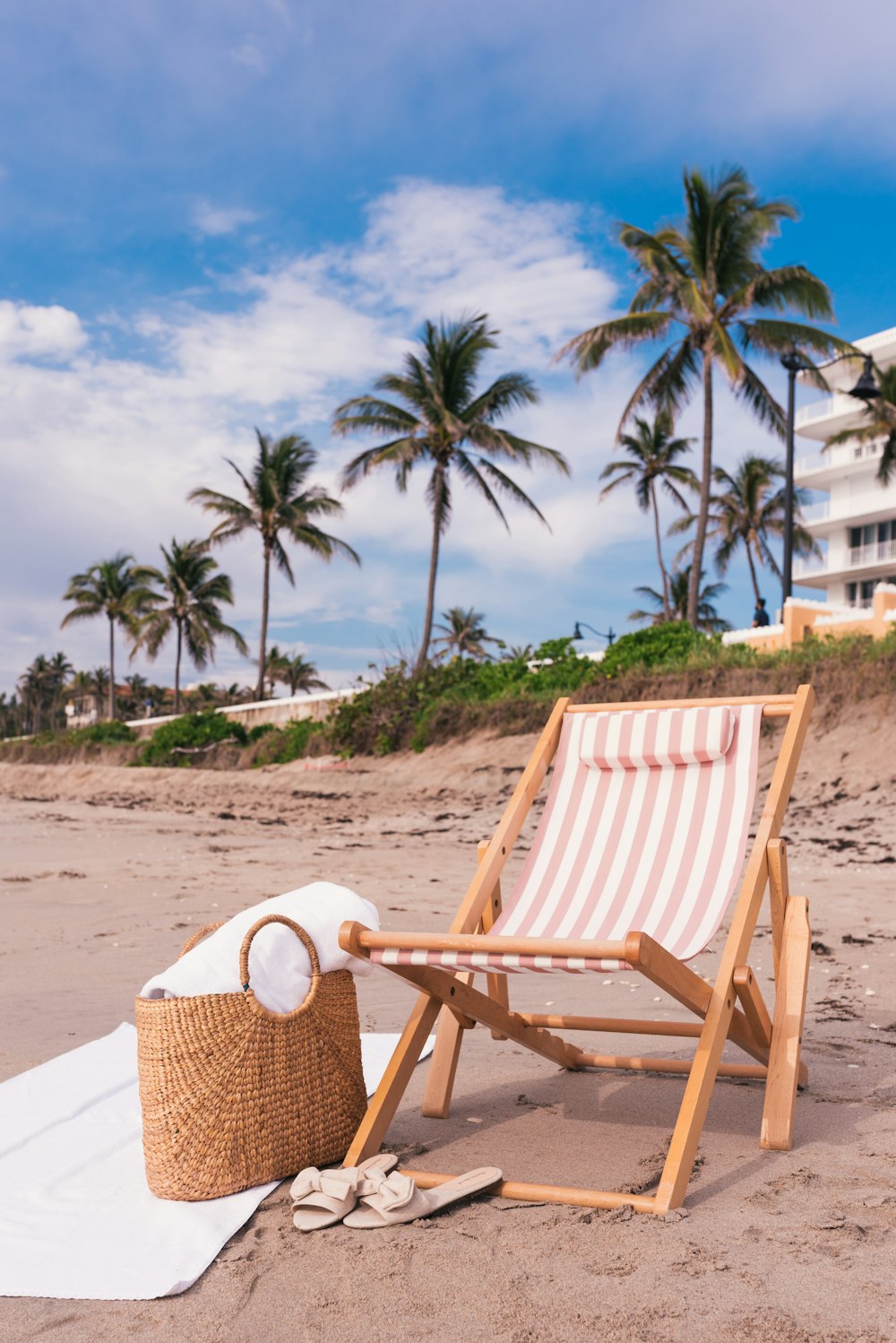 brown wicker basket near white flat sandals and beach chair on seashore under white and blue sky