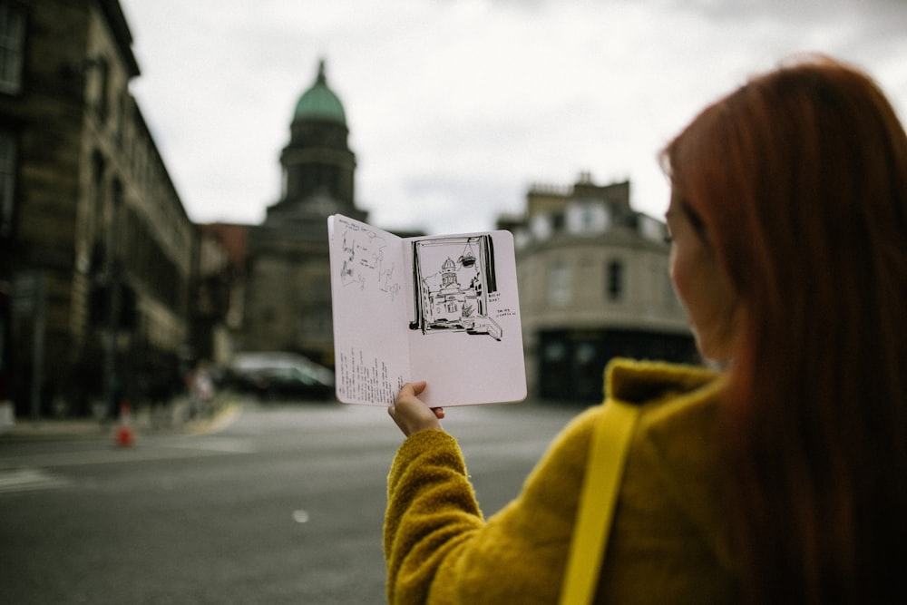 woman wearing yellow jacket standing while holding booklet