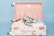 A floral patterned suitcase is open, revealing a pair of stylish loafers with a floral and bird design placed on top of neatly packed clothes. Nearby, a pair of sunglasses rests casually. The interior of the suitcase is lined with a soft pink fabric.