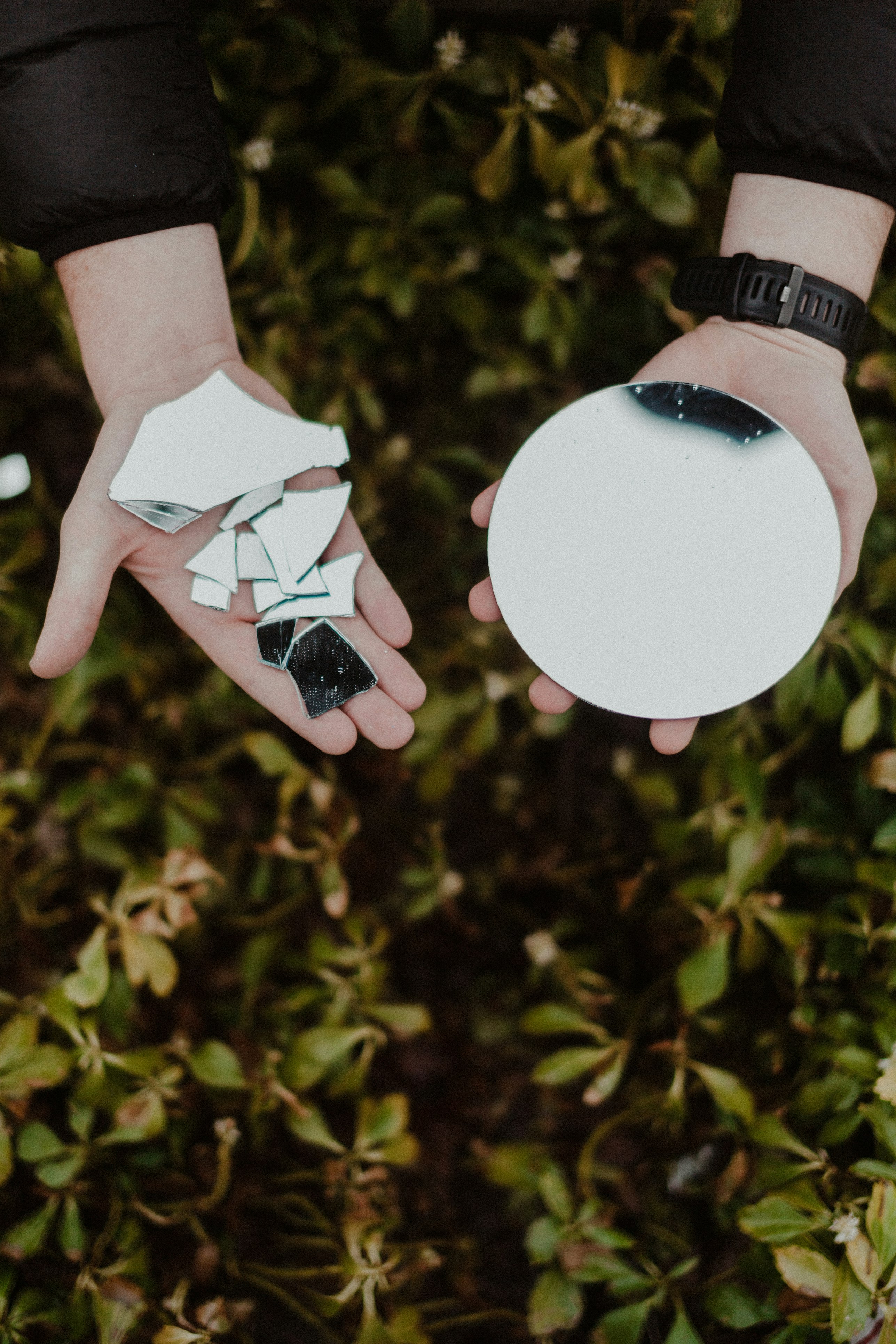 Person with hands extended. In one, mirror shards. In the other, a complete round mirror. Photo by Jeremy Yap.