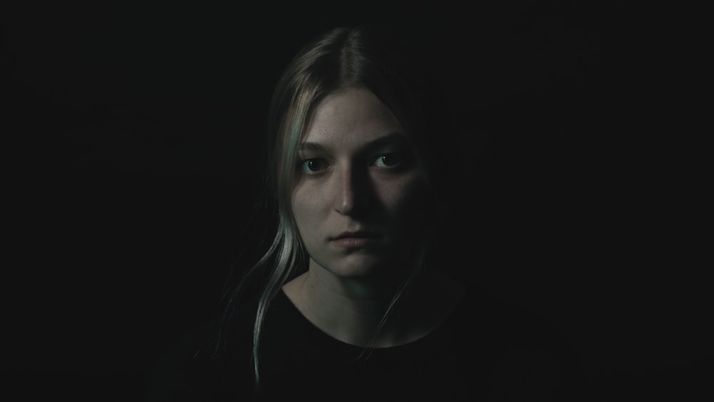 uma mulher em um quarto escuro olhando para a câmera