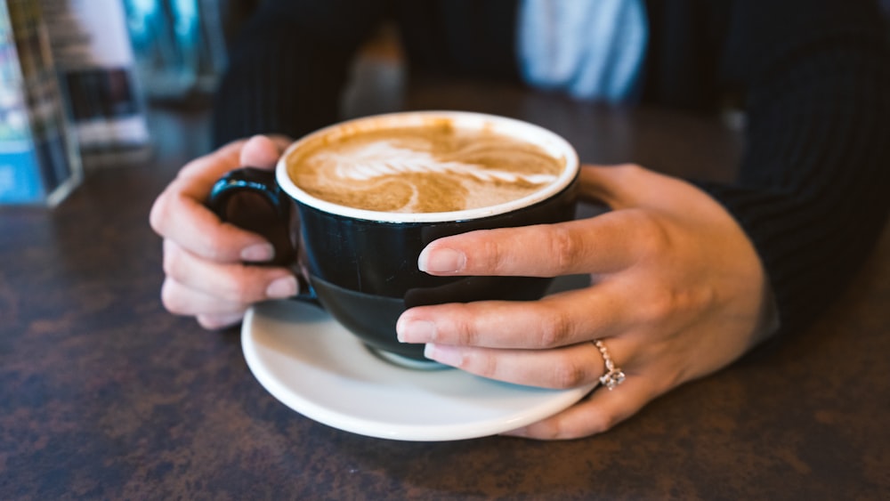 person holding black ceramci cappucino mug with white saucer