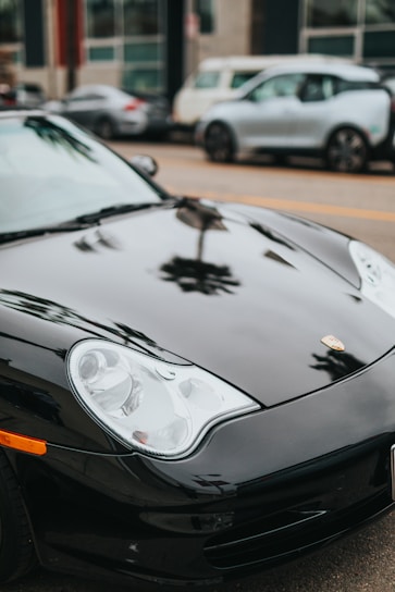 A sleek black luxury sports car parked on a sunlit Los Angeles street, reflecting the city skyline.