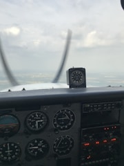 The interior view of an aircraft cockpit displays various flight instruments and gauges, indicating altitude, speed, and orientation. A horizon is visible through the cockpit window, with the sky appearing cloudy.