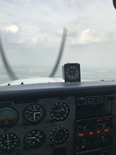 The interior view of an aircraft cockpit displays various flight instruments and gauges, indicating altitude, speed, and orientation. A horizon is visible through the cockpit window, with the sky appearing cloudy.