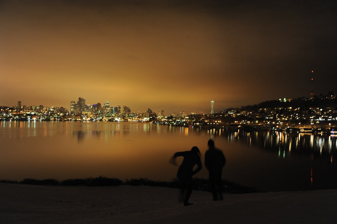 A couple sliding down Meridian Hill, golden glow, snow day, night, winter, Lake Union reflecting lights, Space Needle, Gasworks Park, Seattle, Washington, USA
