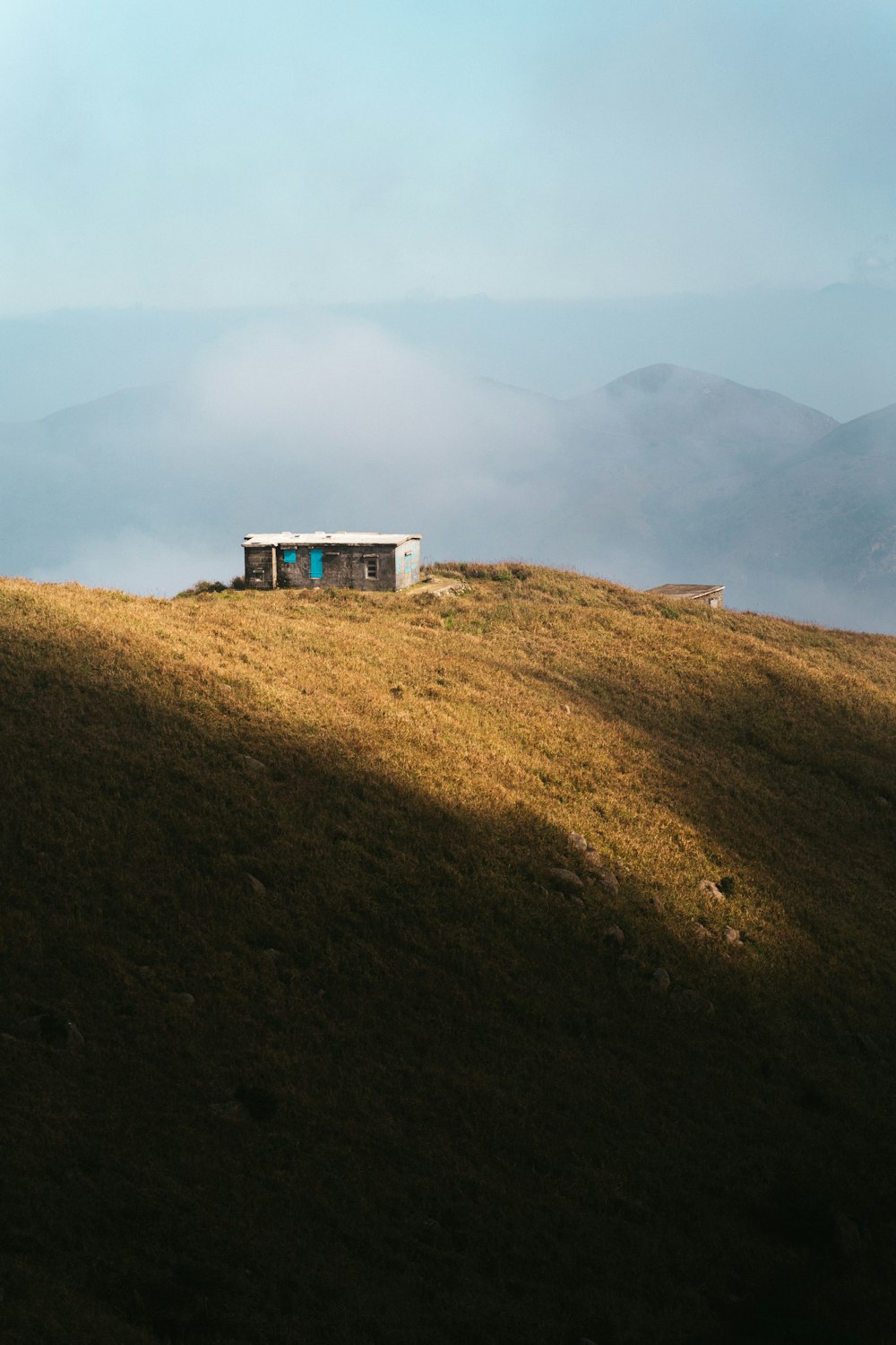 a small hut on a grassy hill with mountains in the background