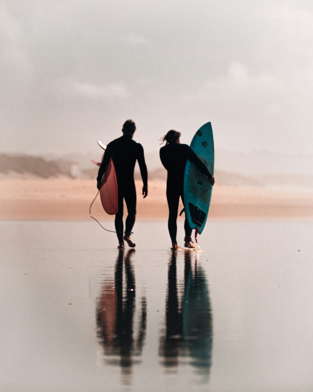 two person holding red and blue surfboards during daytime
