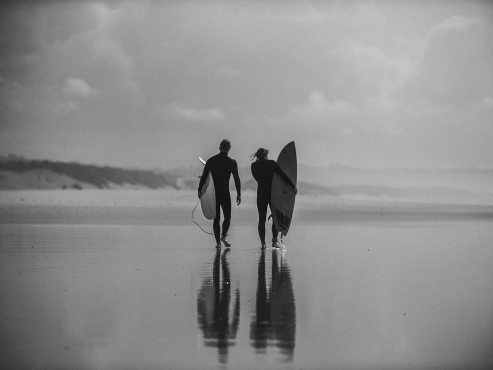 two person walking on beach with surfboards