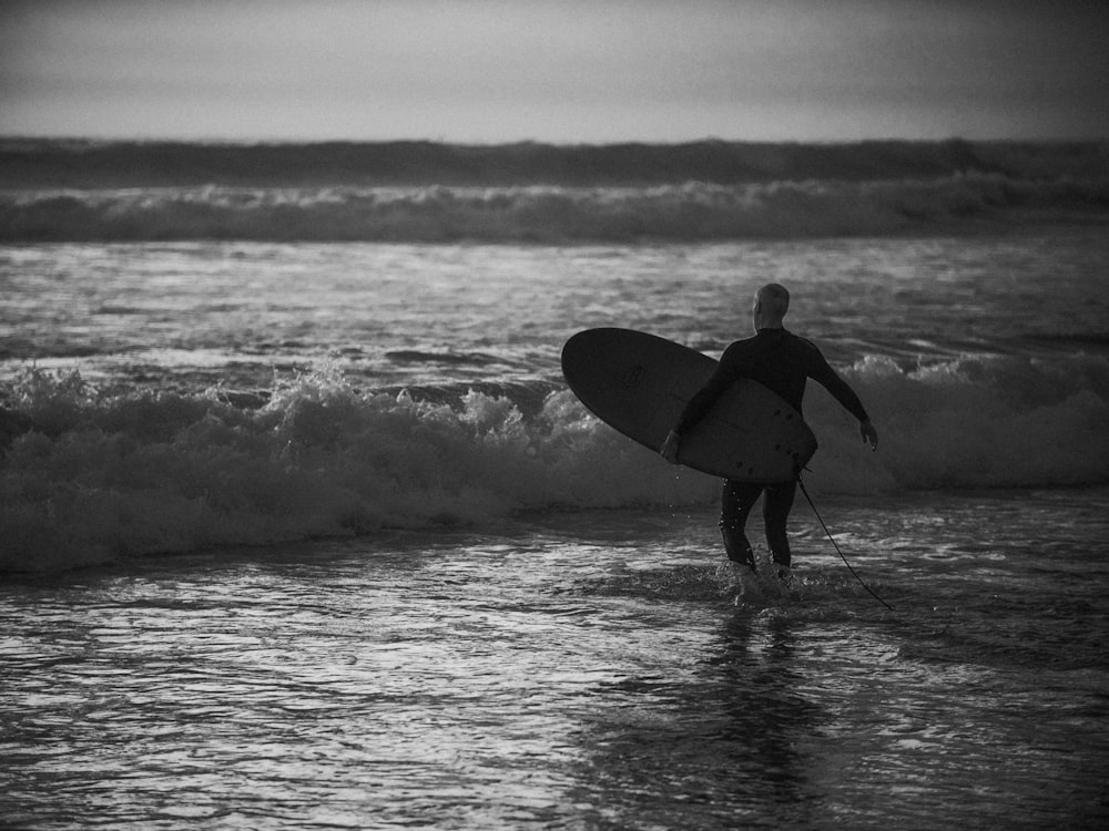 grayscale photography of man holding surfboard during daytime