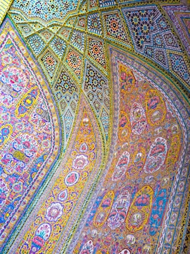 Intricate and colorful mosaic patterns cover the arched ceilings and walls, featuring detailed floral and geometric designs. The artwork combines vibrant hues and ornate craftsmanship, reflecting traditional art styles.